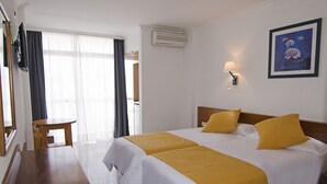 Ett hotellrum med två sängar, ett skrivbord i trä, en stol och ett stort fönster med gardiner.