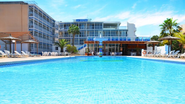 Ett hotell med en swimmingpool, solstolar och en palm.