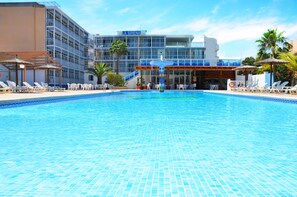 A hotel with a swimming pool, sun loungers, and a palm tree.