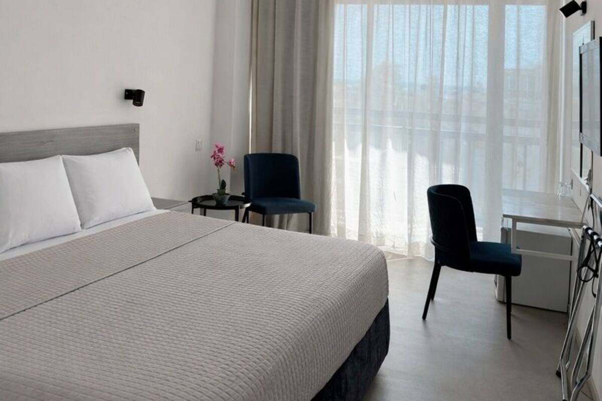 A hotel room with a large bed, a desk with a chair, a TV, and a window with curtains.