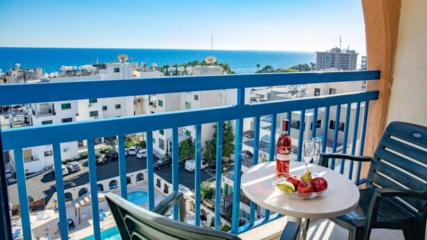 Un balcon avec une table dressée pour deux personnes, offrant une vue sur le paysage urbain et la mer.