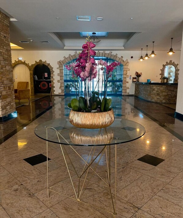 Un vestíbulo con una mesa de vidrio, un arreglo floral, arcos de piedra y una recepción.