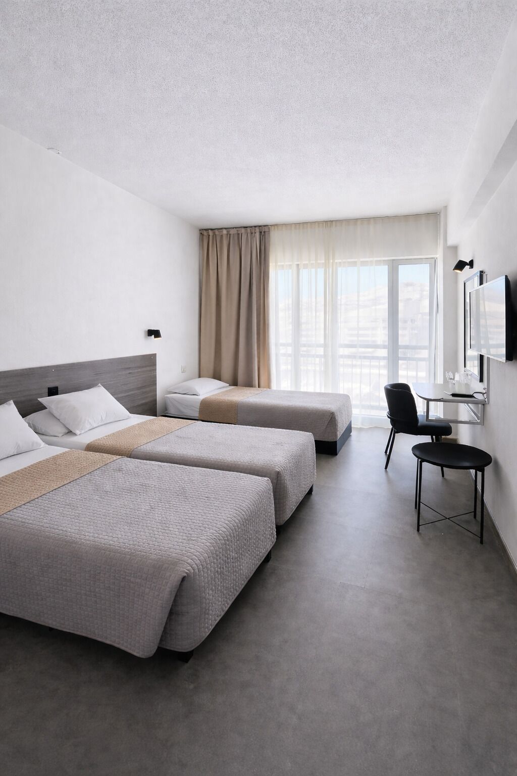 Habitación de hotel con dos camas, un escritorio, una silla y un ventanal grande.