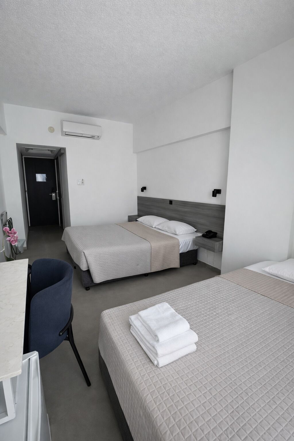 A hotel room with two beds, a desk, a chair, and an air conditioning unit.