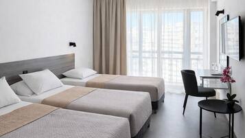 Habitación de hotel con dos camas, un escritorio, una silla y un ventanal con cortinas.