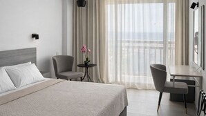 Une chambre d’hôtel avec un lit, un bureau, une chaise, une petite table ornée de fleurs et une vue sur l’extérieur.
