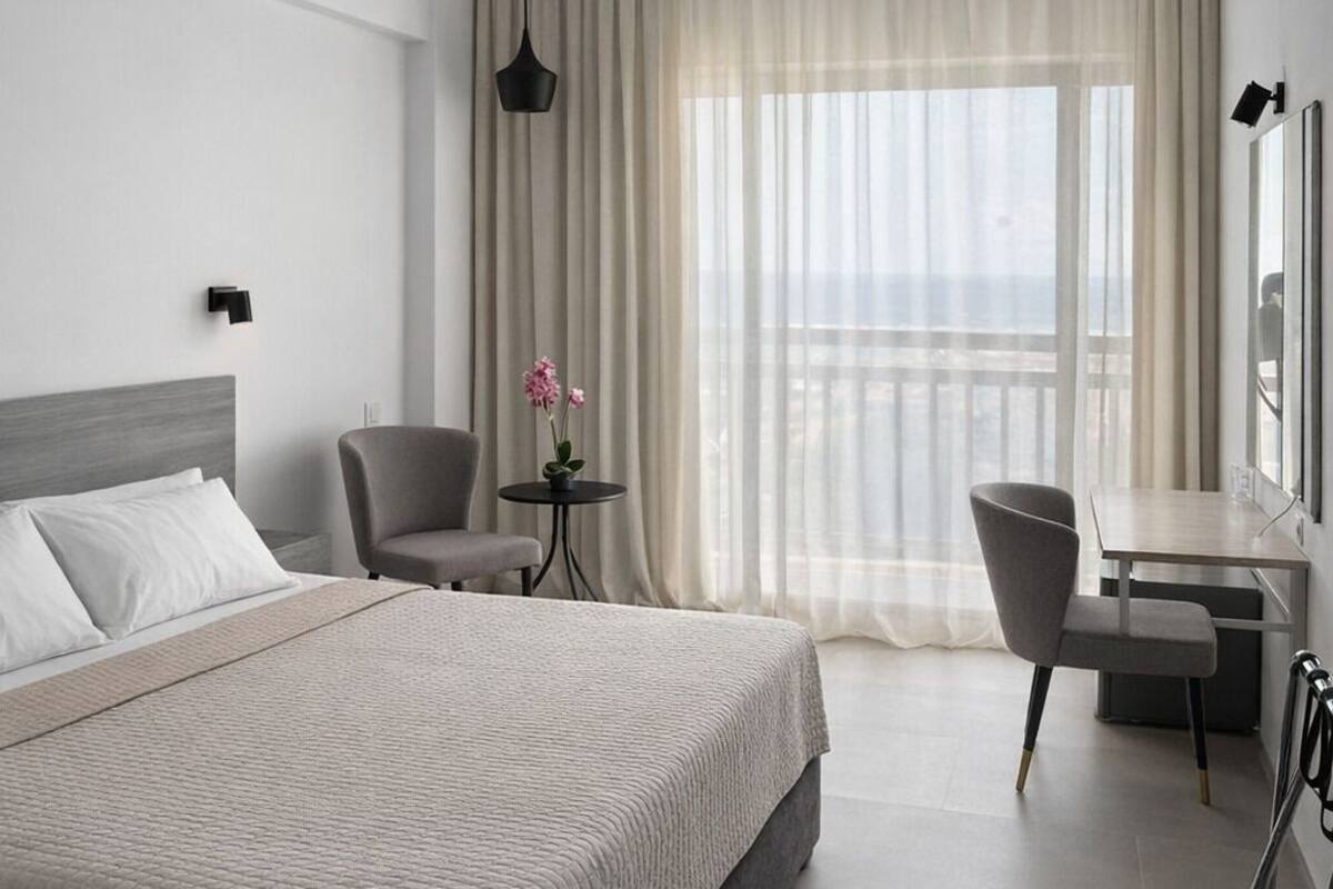 A hotel room with a bed, a desk, a chair, a small table with flowers, and a view of the outside.
