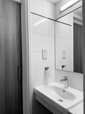A modern bathroom with a white sink, a mirror, and a wooden door.