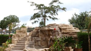 Une formation rocheuse surmontée d’un escalier, entourée de plantes en pot et d’un arbre.