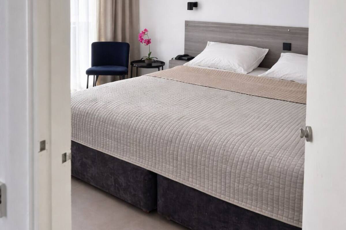 A bedroom with a bed, a nightstand, a chair, and a window with curtains.