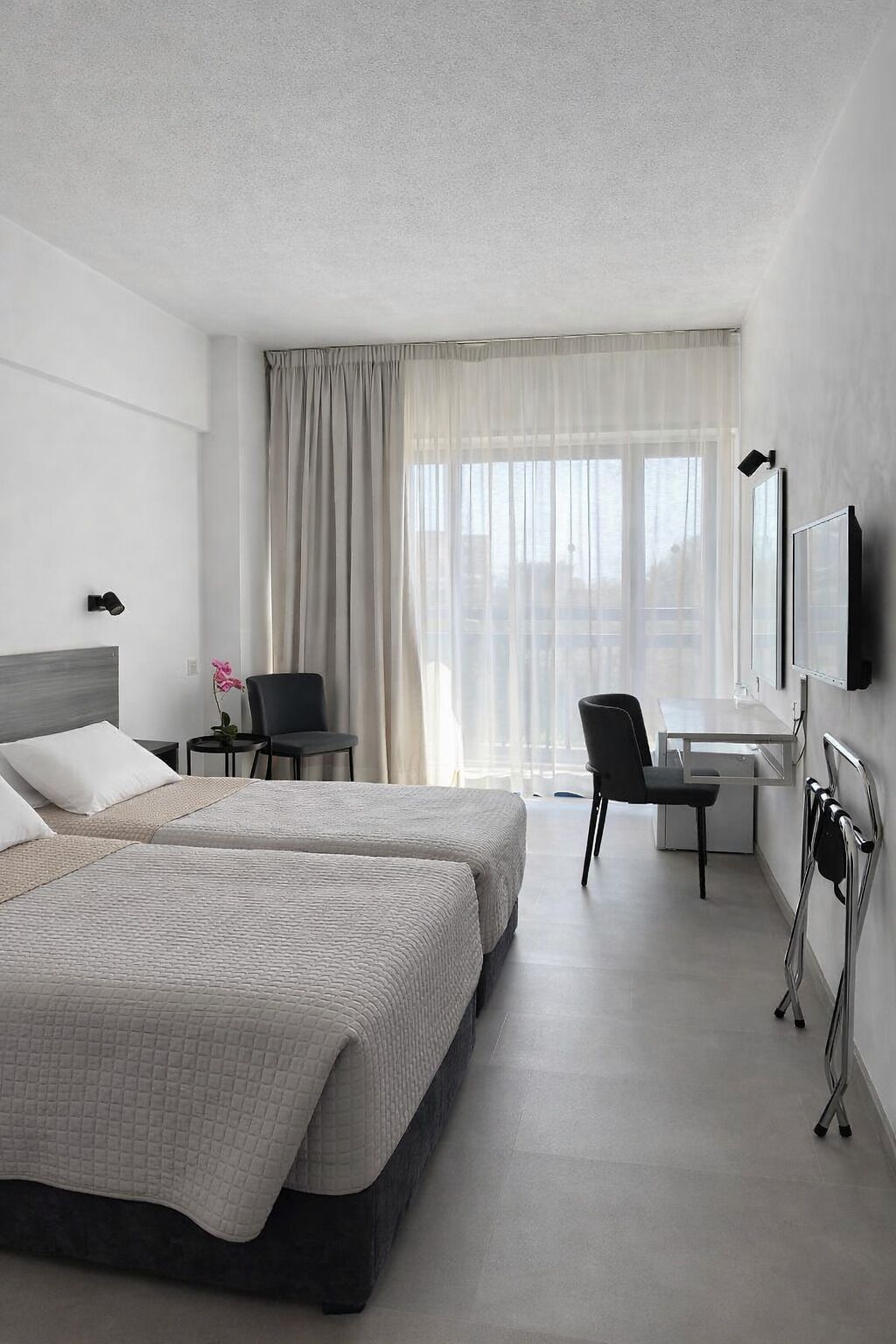 A modern hotel room with two beds, a desk, a chair, a TV, and a window with curtains.