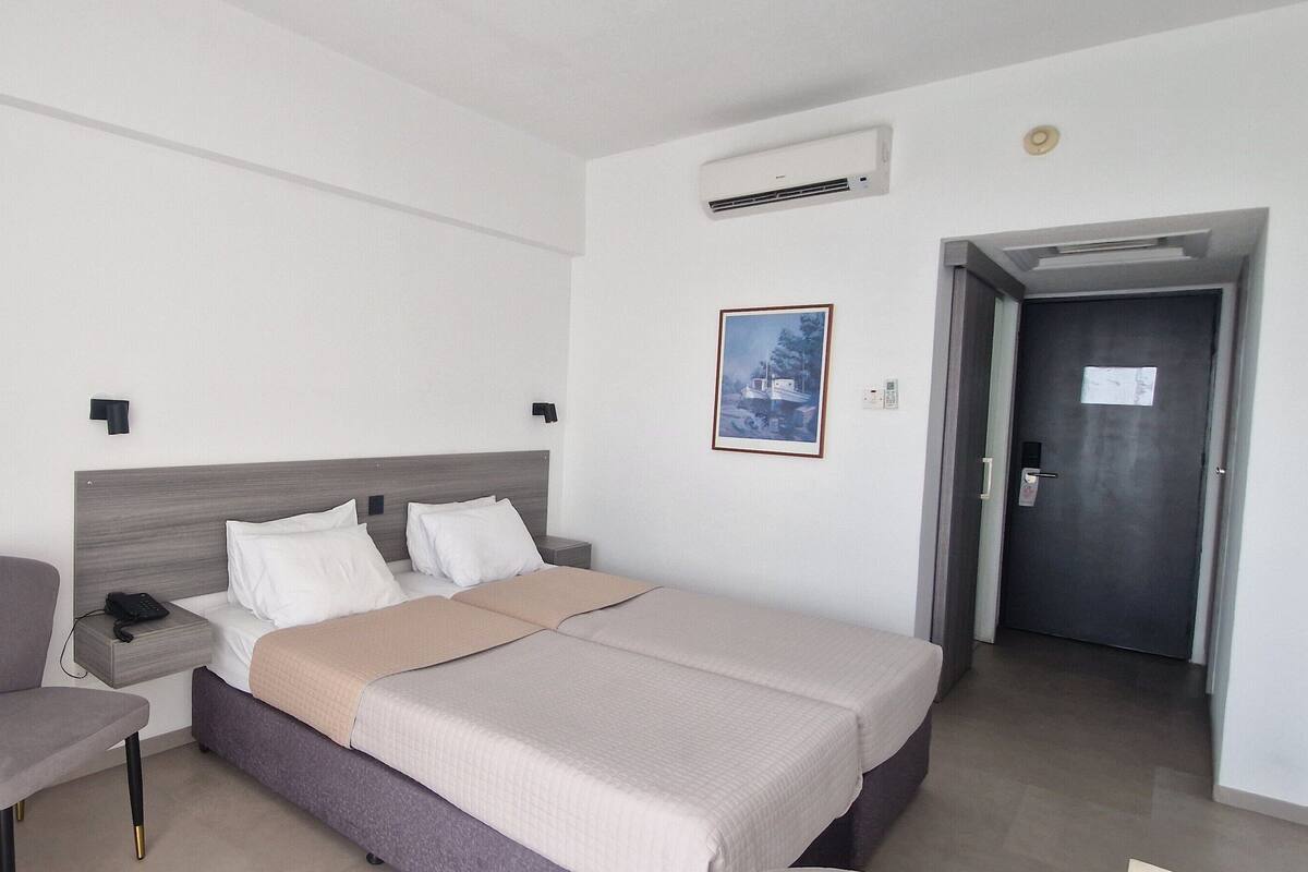 A hotel room with a bed, bedside table, chair, and a small table with a potted plant.