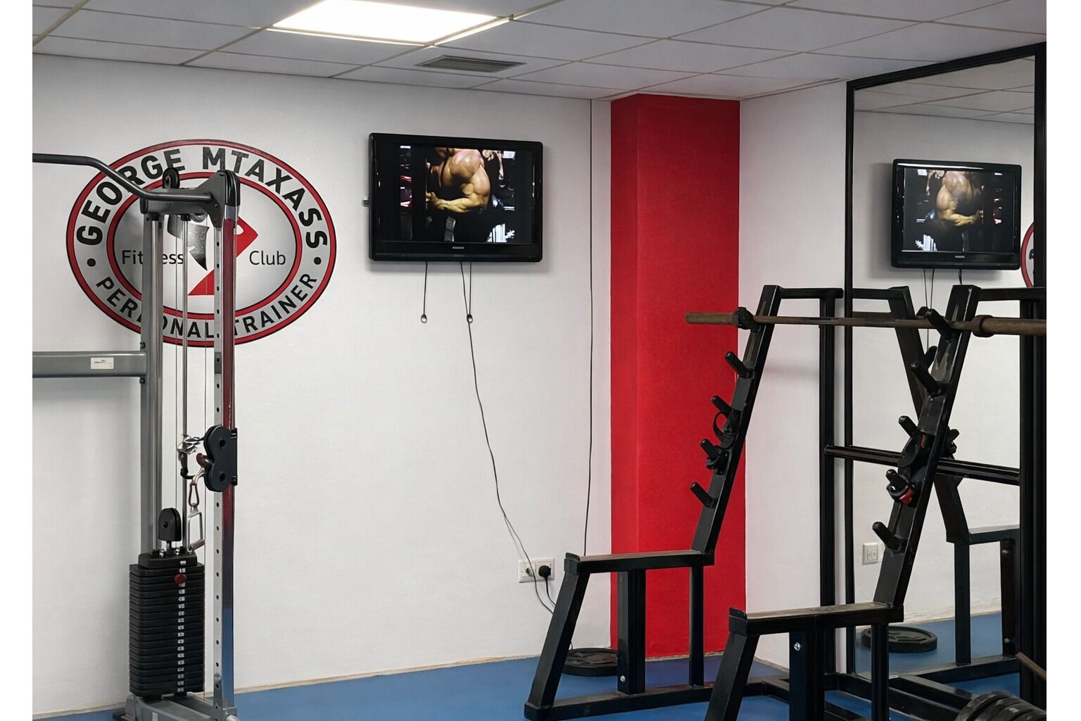 A gym with exercise equipment, a television, and a red wall.