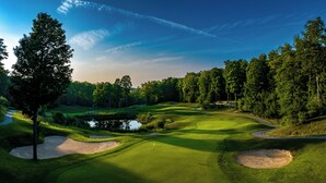 Een golfbaan met zandbunkers, een vijver en een vlaggenstok.
