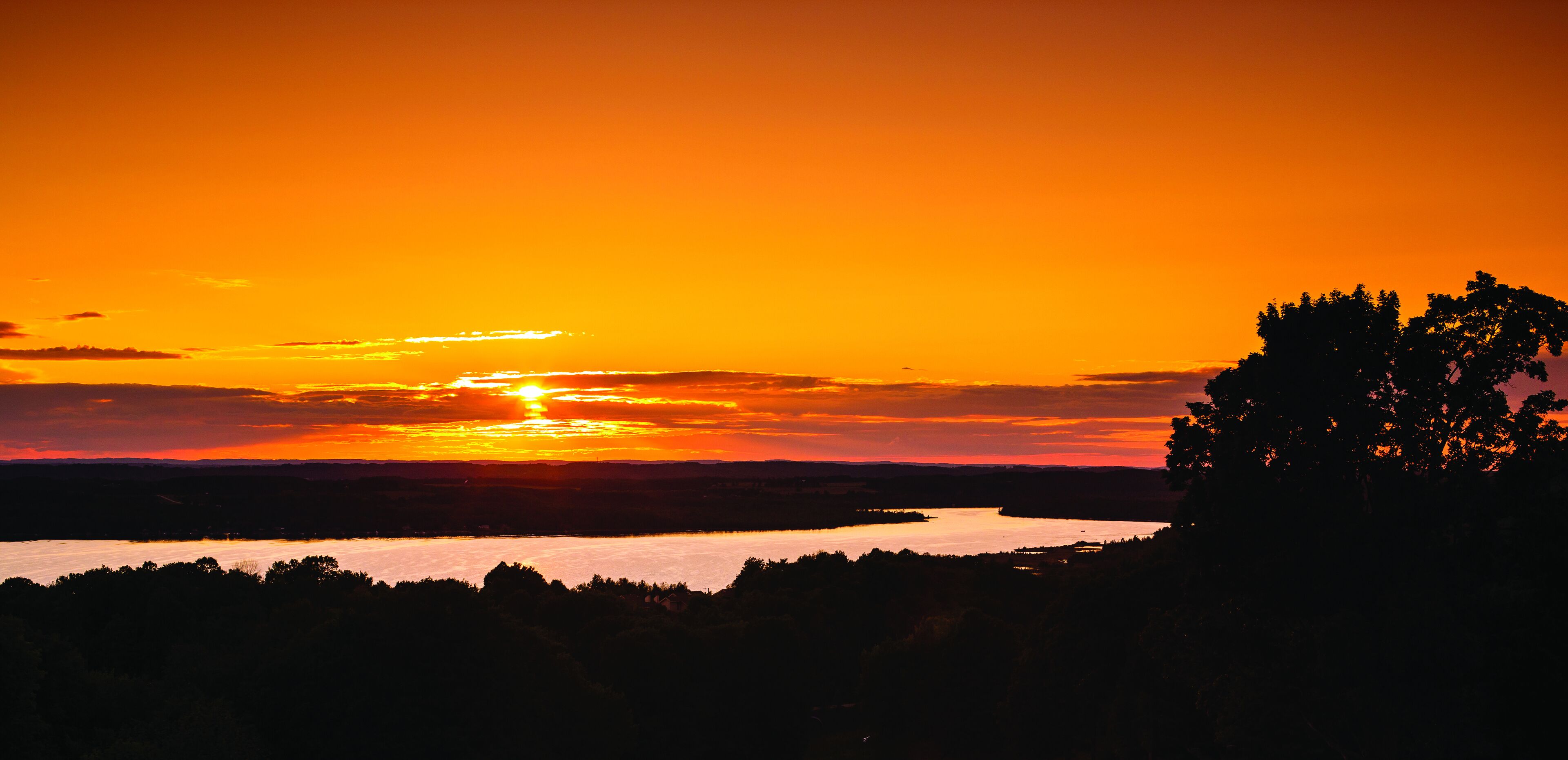 A sunset over a lake with trees silhouetted against the sky.