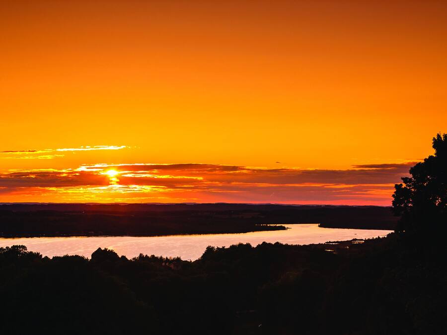 Ein See im Sonnenuntergang, Bäume sind als Silhouette am Himmel erkennbar.