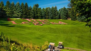 A golf course with a large, red and green text spelling "The Legend" on the grass, surrounded by trees and two golf carts.