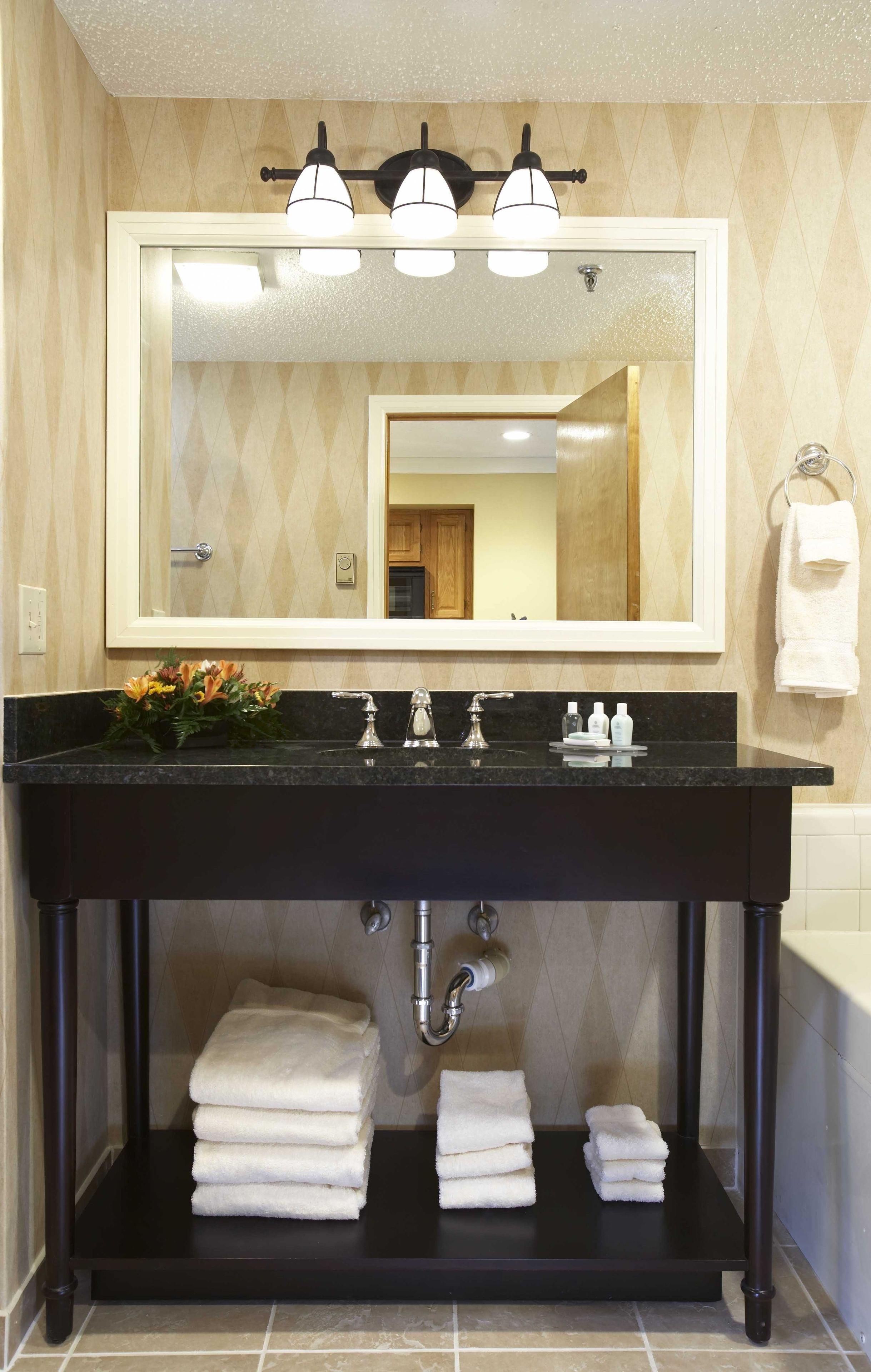 Une salle de bain avec un meuble-lavabo noir, un grand miroir, trois luminaires et un porte-serviettes.