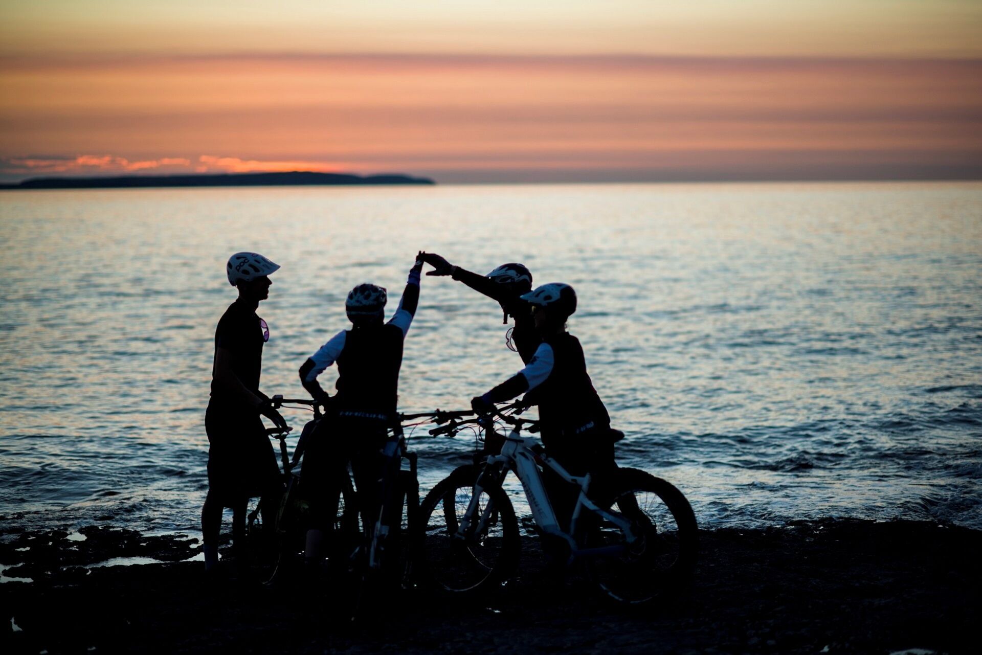A group of cyclists silhouetted against a sunset by the water.