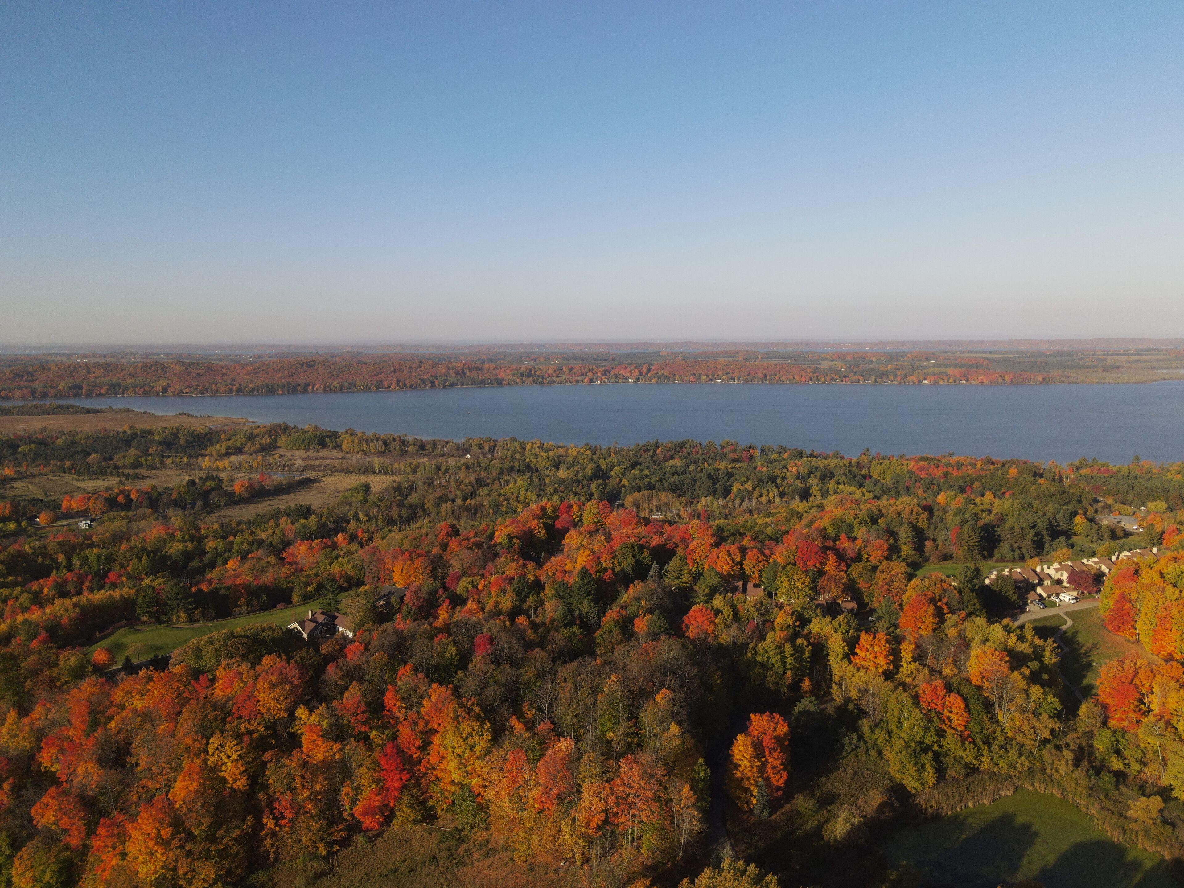 Une vue panoramique d’une zone au bord d’un lac, avec le feuillage automnal, un ciel dégagé et des bâtiments situés au loin.