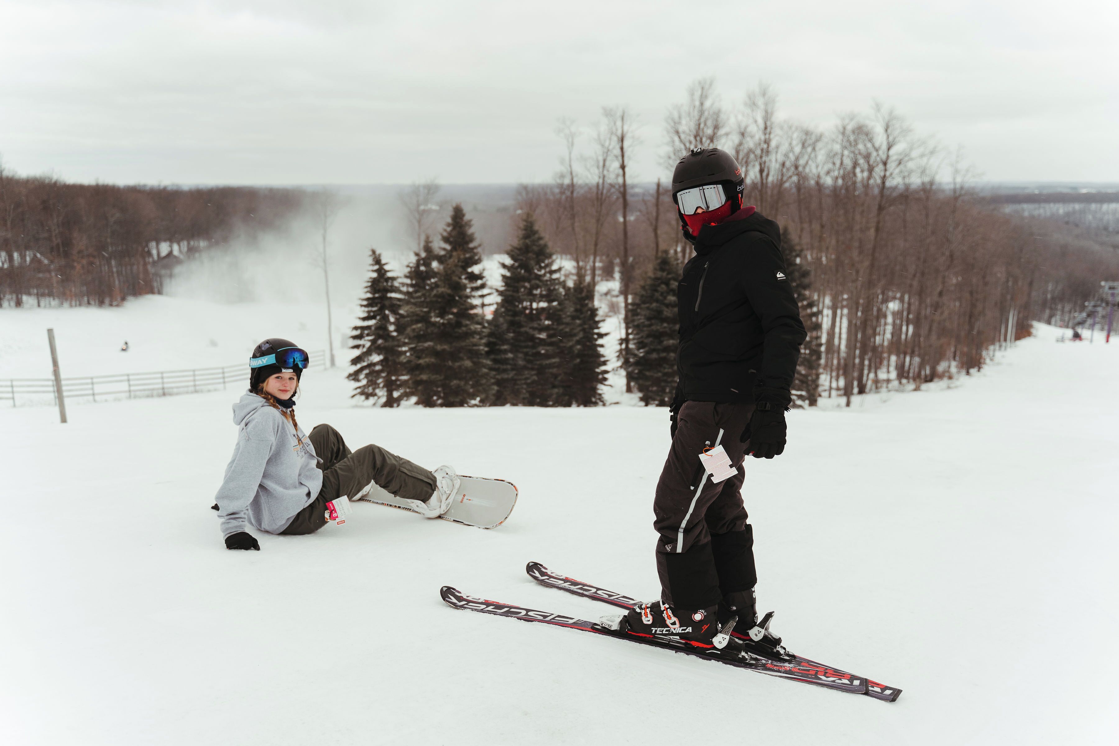 Un paysage enneigé où l’on voit une personne assise par terre et une autre, debout, avec des skis.