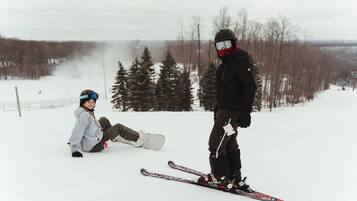 A snowy landscape with a person sitting on the ground and another standing with skis.