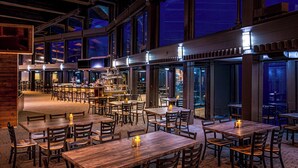 Een ruime restaurant met meerdere tafels en stoelen, een bar en grote ramen met uitzicht op de skyline.