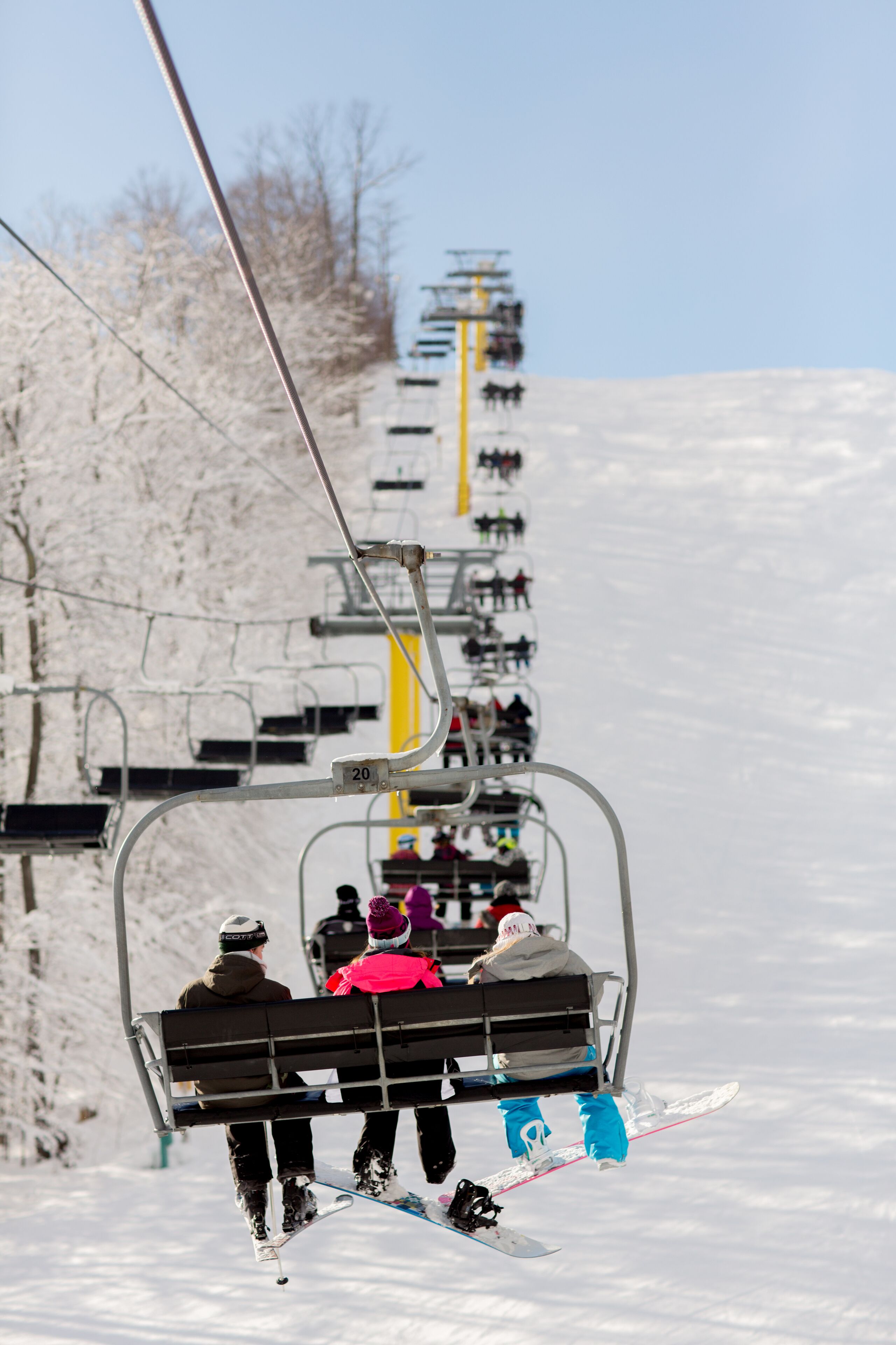 Teleférico de esqui com passageiros, árvores cobertas de neve e um céu limpo.