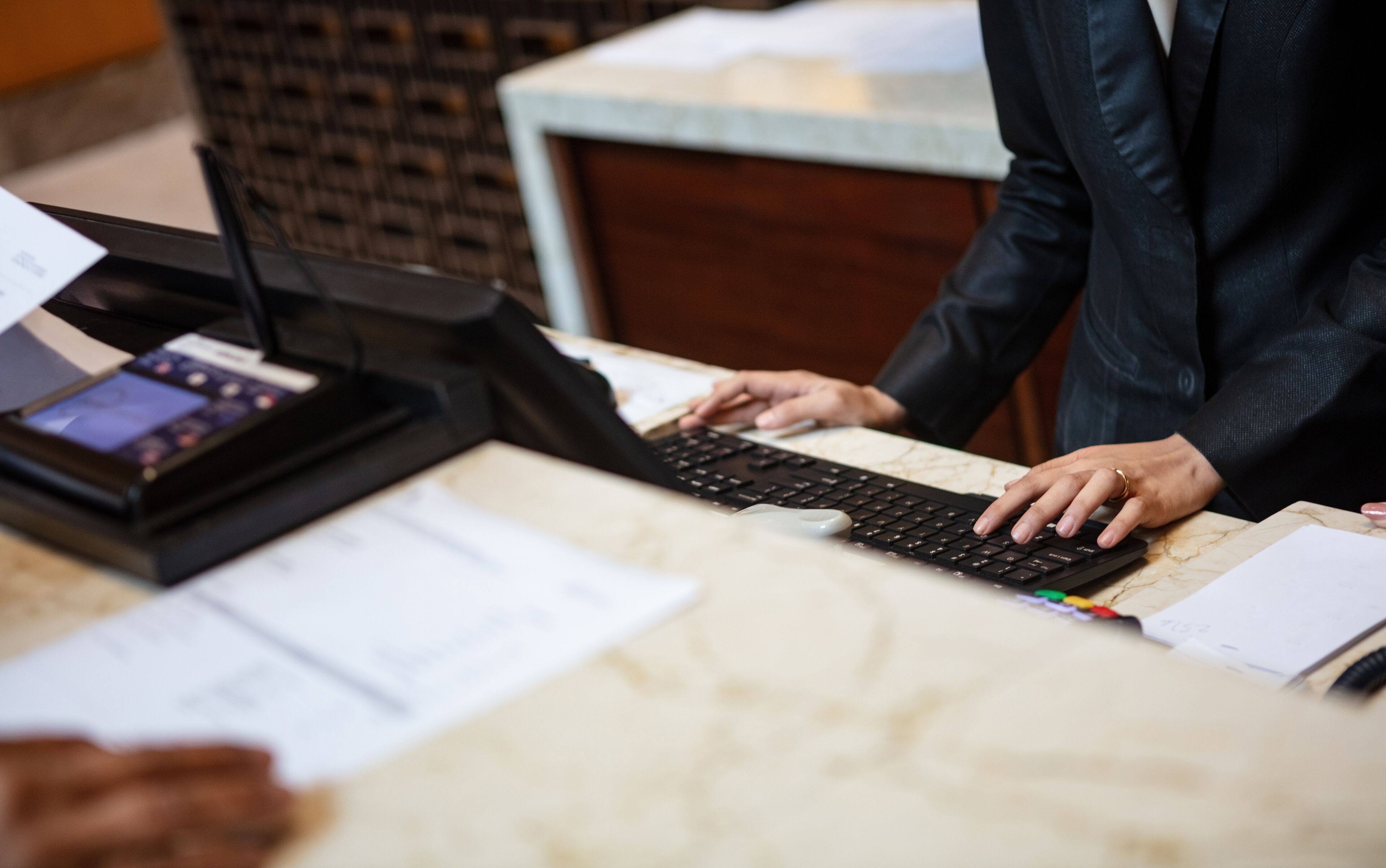 Una persona atendiendo en la recepción, con una computadora, una caja registradora y algunos documentos.