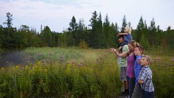 Un groupe de personnes se tient sur une terrasse en bois, au bord d’un lac, entouré de grands arbres et de fleurs sauvages.