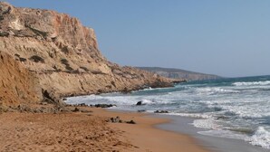 Una playa arenosa con acantilados rocosos y olas rompiendo en la orilla.