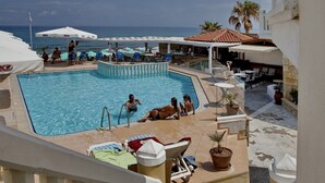 A pool area with lounge chairs, umbrellas, and a view of the sea. - Jo-An Beach Hotel (Rethymno)