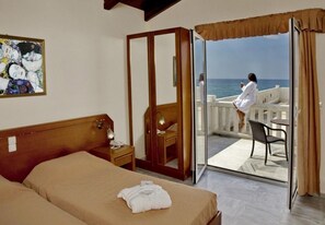 A hotel room with a bed, a bedside table, a mirror, and a sliding glass door leading to a balcony with a view of the sea. - Jo-An Beach Hotel (Rethymno)