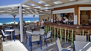 An outdoor seating area with tables and chairs, a bar, and a view of the sea. - Jo-An Beach Hotel (Rethymno)