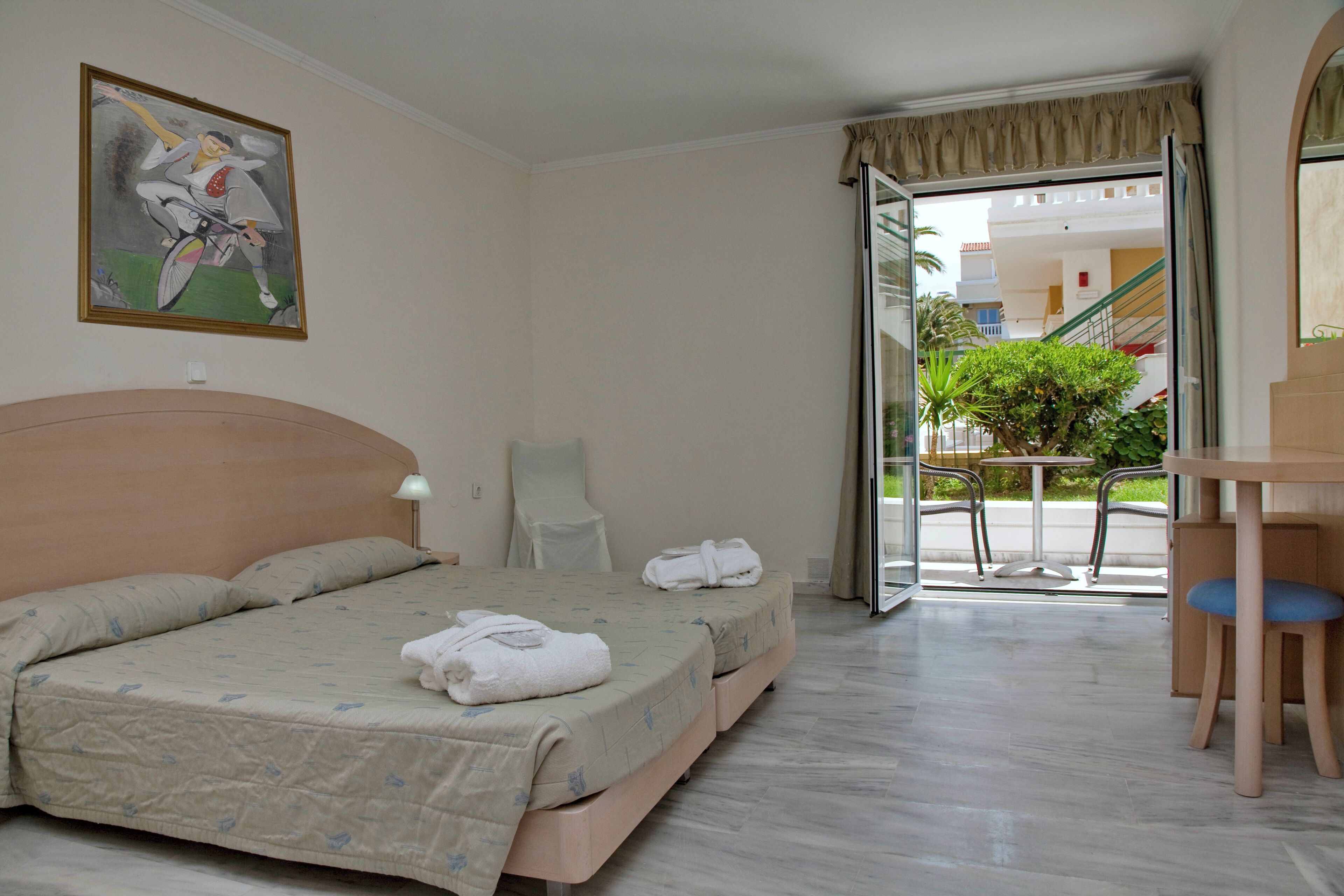 Una habitación de hotel con cama, una silla, una mesa y un cuadro en la pared.