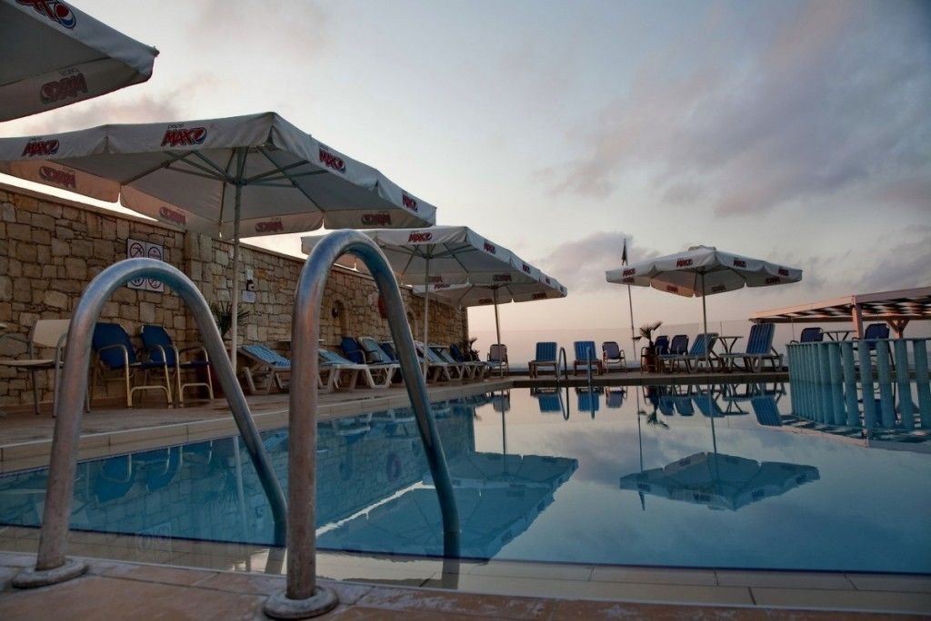 A pool area with lounge chairs and umbrellas, stone walls, and a clear sky.