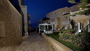 A stone-paved courtyard with buildings on either side, a covered seating area, and a well-maintained garden. - Jo-An Beach Hotel (Rethymno)