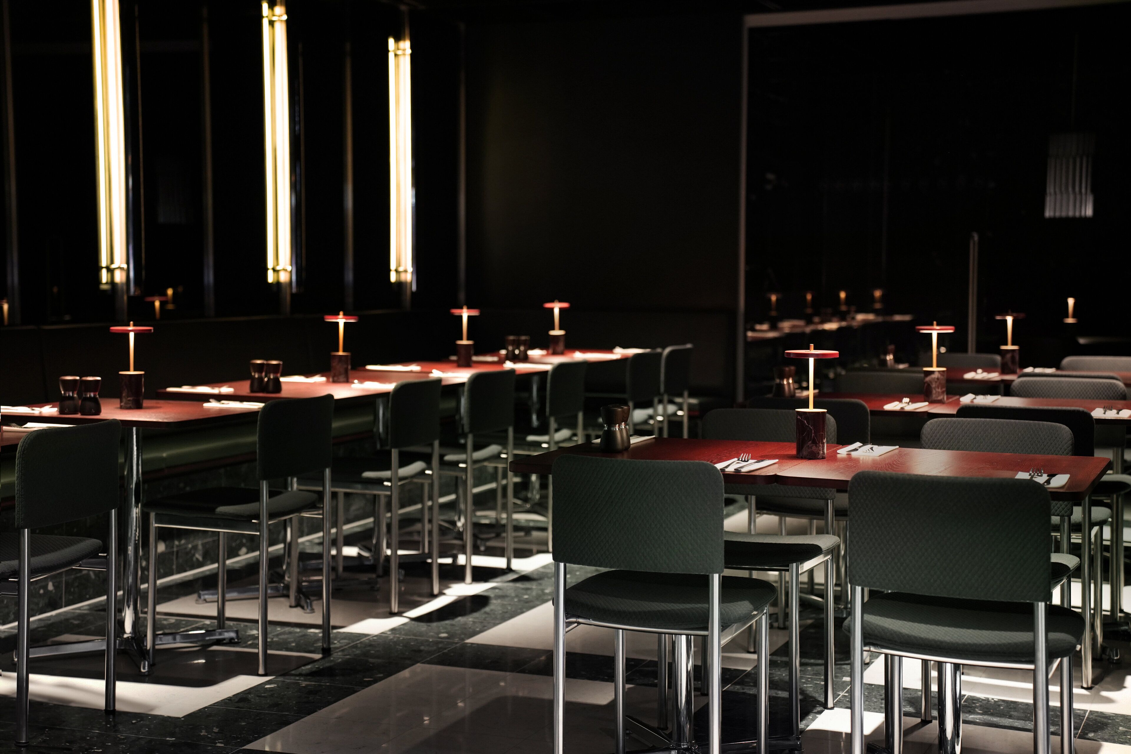 A restaurant with multiple tables and chairs, illuminated by vertical light fixtures.