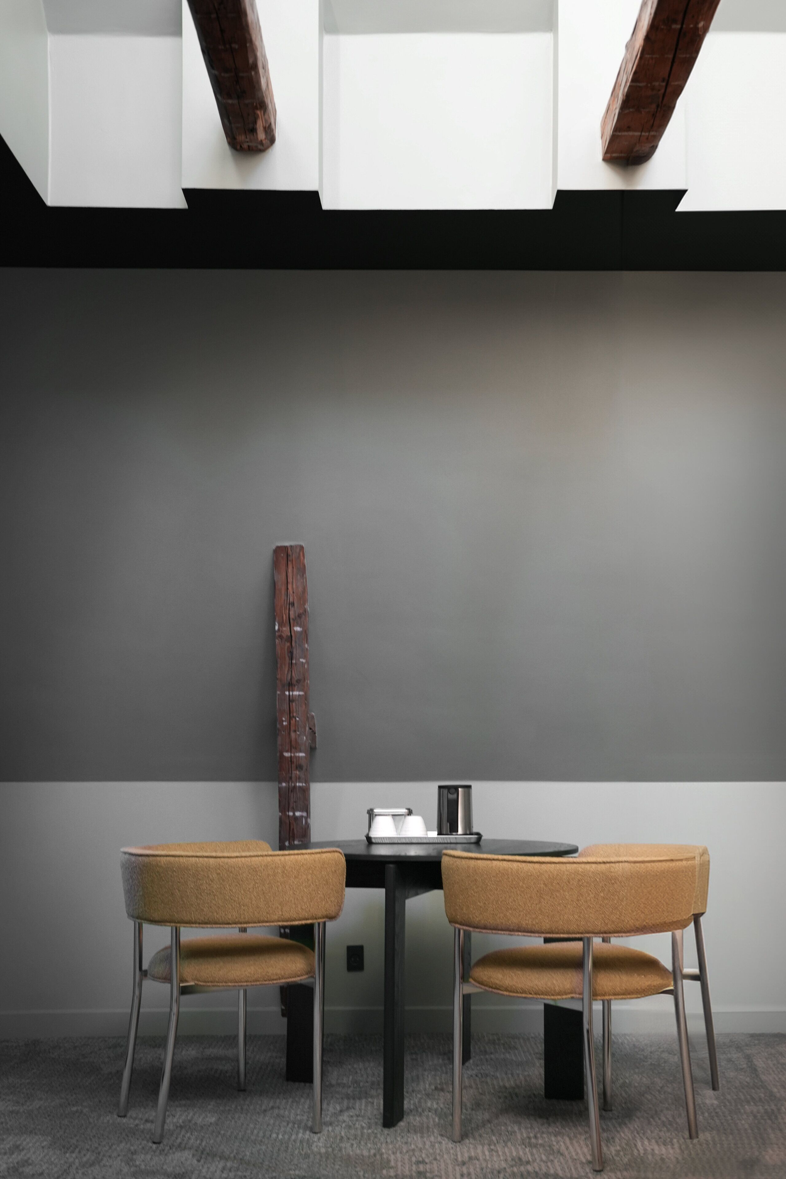 Ein modernes Zimmer mit grauer Wand, einem Holzdetail, einem schwarzen Tisch und zwei Stühlen.