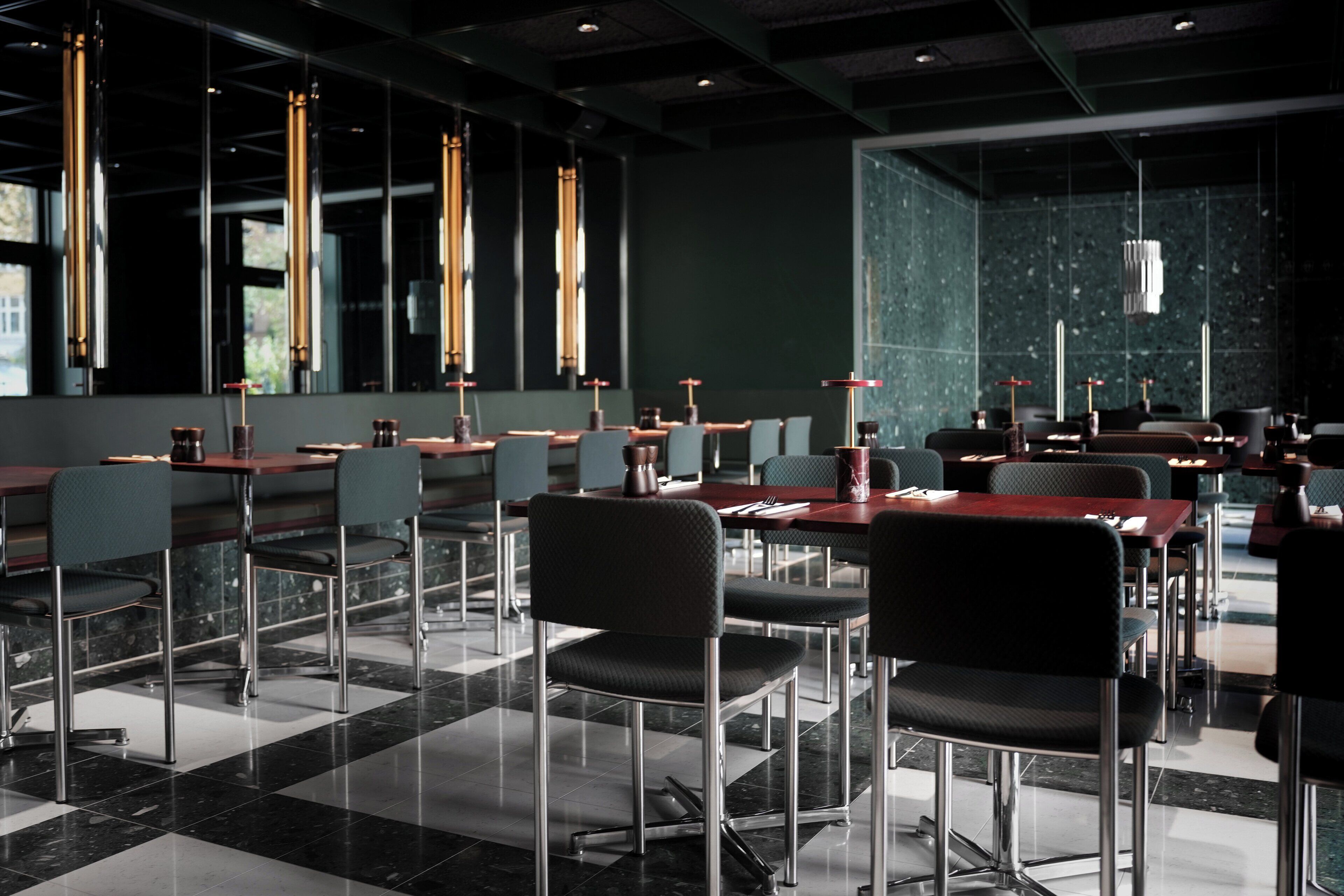 Un restaurante moderno con mesas y sillas altas, ventanas amplias e iluminación colgante.
