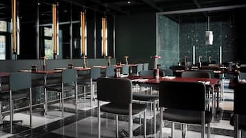 Un restaurante moderno con mesas y sillas altas, ventanas amplias e iluminación colgante.