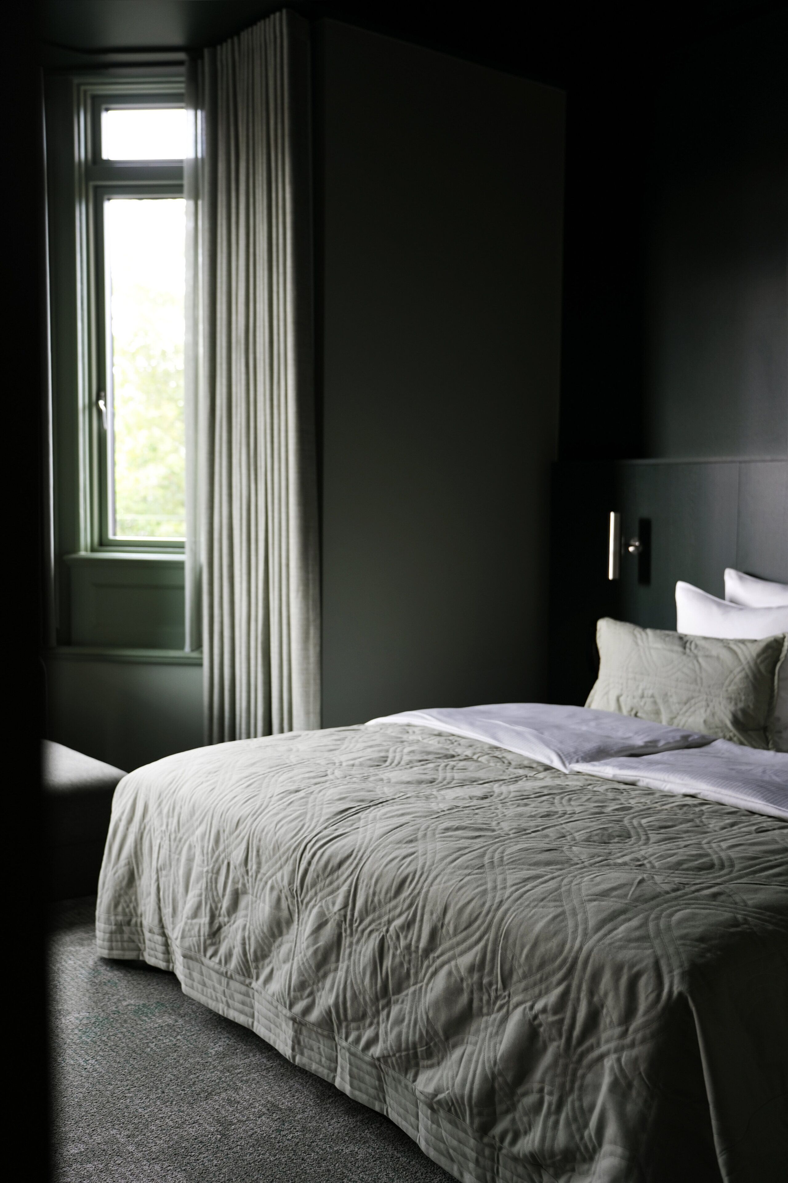 A bedroom with a large bed, a window with curtains, and a dark wall.