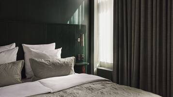 Una cama bien hecha con almohadas blancas y verdes, un cabecero verde oscuro y una mesita de noche con una lámpara roja.