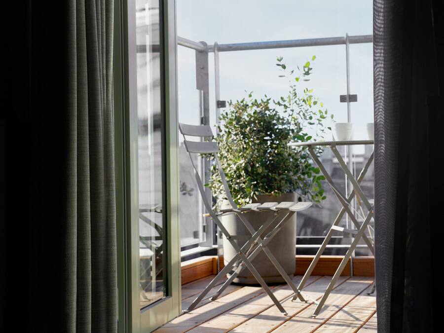 A balcony with a potted plant, a metal chair, and a wooden floor.