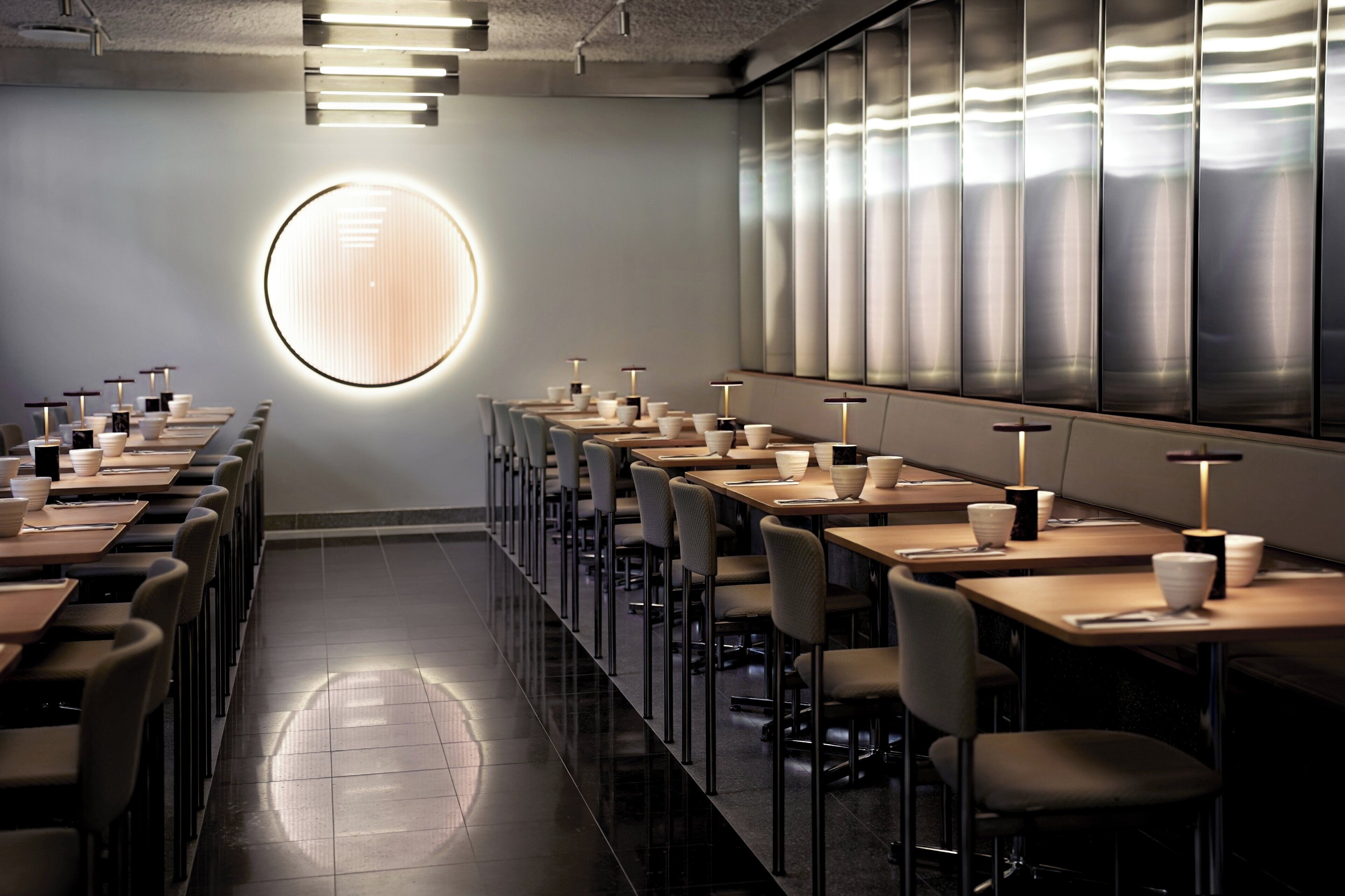Un comedor moderno con mesas largas, sillas y apliques redondos en la pared.