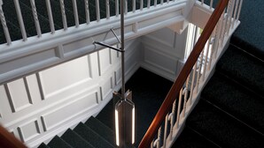 A staircase with white railings and a wooden handrail, leading to a landing with a view of greenery outside. - Boutique Hotel Hans (Frederiksberg)