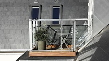 Terraço no telhado com planta em vaso, uma mesa pequena e duas janelas.