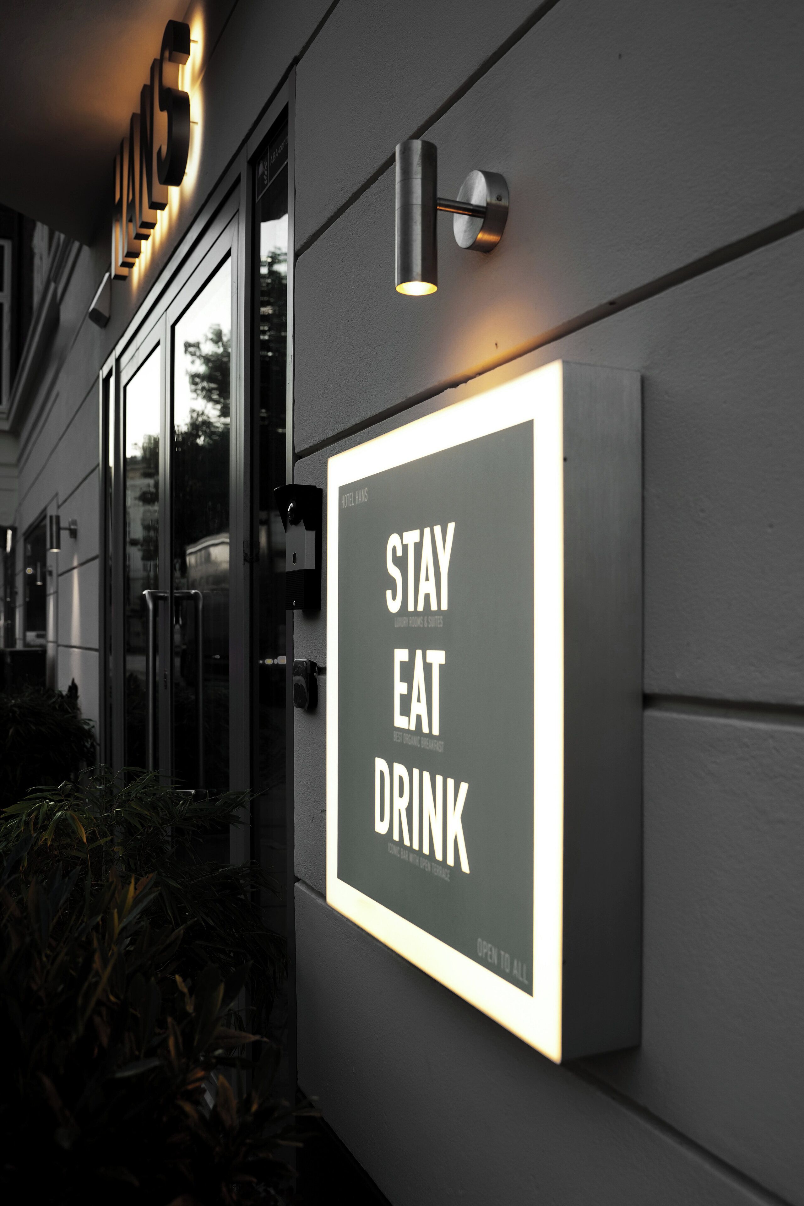 A sign on a building wall that reads "STAY EAT DRINK OPEN TO ALL."