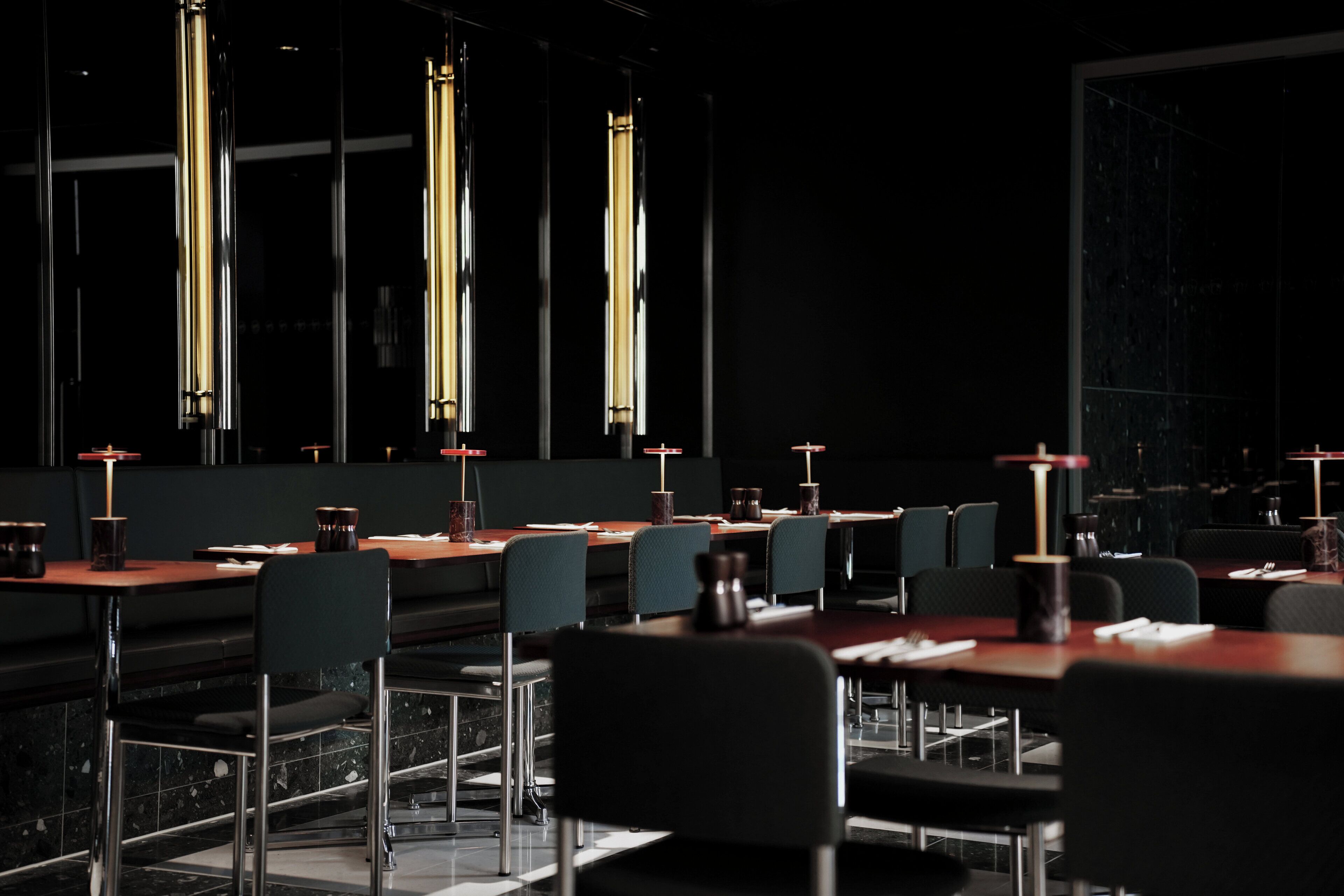 Un restaurante moderno con mesas y sillas altas, iluminación colgante y un interior oscuro.