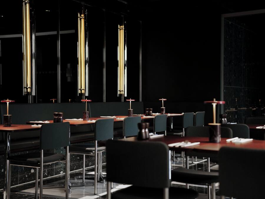 Un restaurante moderno con mesas y sillas altas, iluminación colgante y un interior oscuro.